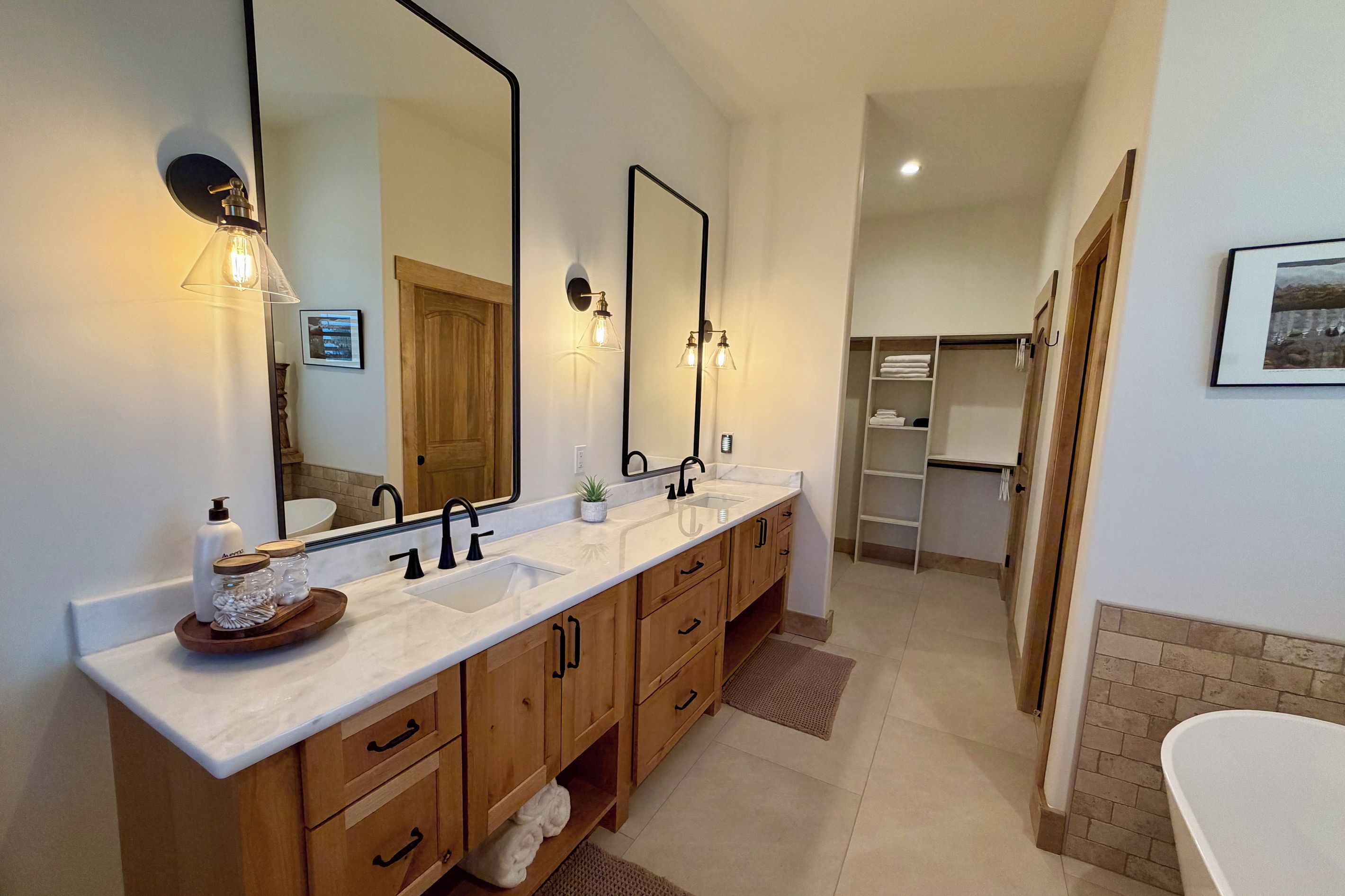 A modern bathroom with a double sink vanity, wooden cabinets, a large mirror, and a walk-in shower.