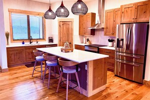 A modern kitchen with wooden cabinets, a stainless steel refrigerator, and a bar area with stools. - The Oar Lock Cottage (Ennis)
