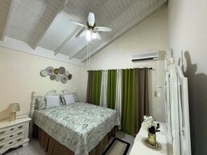 Ein Schlafzimmer mit einem Bett, einem Nachttisch, einer Kommode, einem Deckenventilator und einer Wand-Klimaanlage.