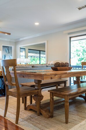 A dining area with a wooden table, chairs, and a bench. There is a bowl on the table, and the room has large windows. - Lake Views | Two King Suites | Pool Access (Hot Springs)