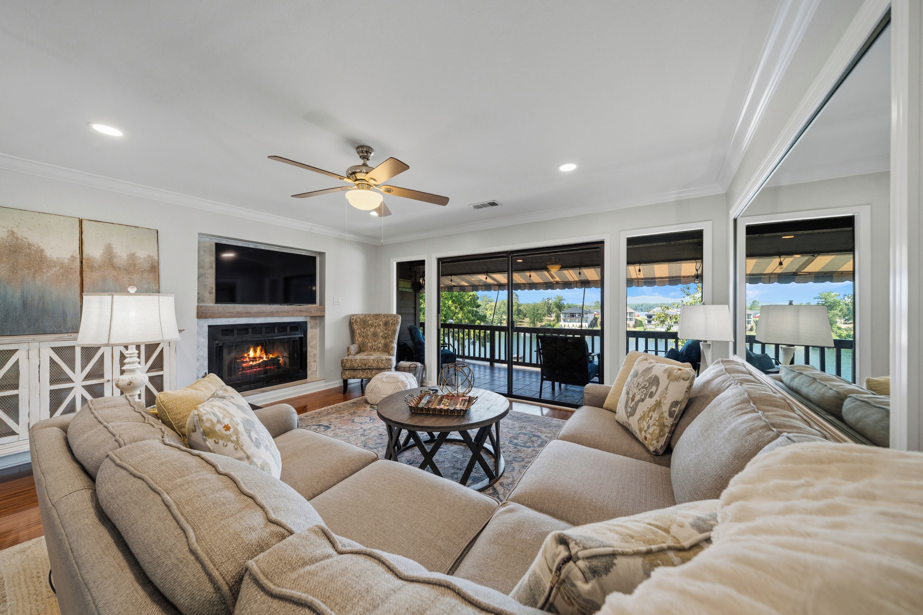 A spacious living room with a fireplace, comfortable seating, and a view of a lake.
