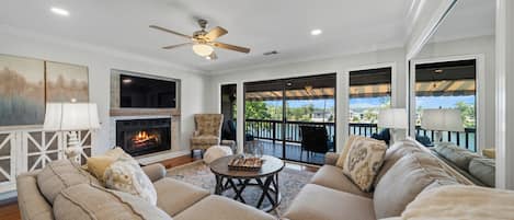 A spacious living room with a fireplace, comfortable seating, and a view of a lake.