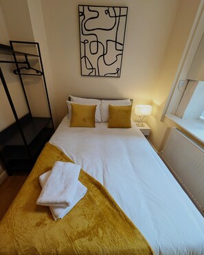 Une chambre d’hôtel comprenant un lit, une table de chevet avec une lampe, un porte-manteau mural et une œuvre d’art décorative.