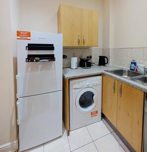 Une cuisine compacte équipée d’un réfrigérateur, d’un lave-linge et de meubles de rangement en bois.