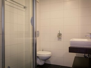 Ein Badezimmer mit Duschkabine aus Glas, einer weißen Toilette und einem Waschbecken mit dunkler Arbeitsplatte.