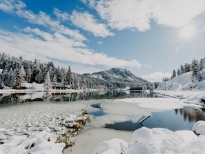 Paisagem de inverno com um lago congelado, árvores cobertas de neve e uma montanha ao fundo.