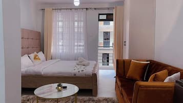 Un dormitorio con cama, una mesita de centro redonda, un sofá y vista a un balcón exterior.