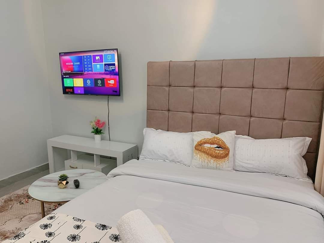 A modern bedroom with a large bed, a mounted TV, a bedside table, and a small round table with a plant.