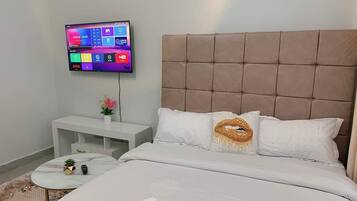 A modern bedroom with a large bed, a mounted TV, a bedside table, and a small round table with a plant.