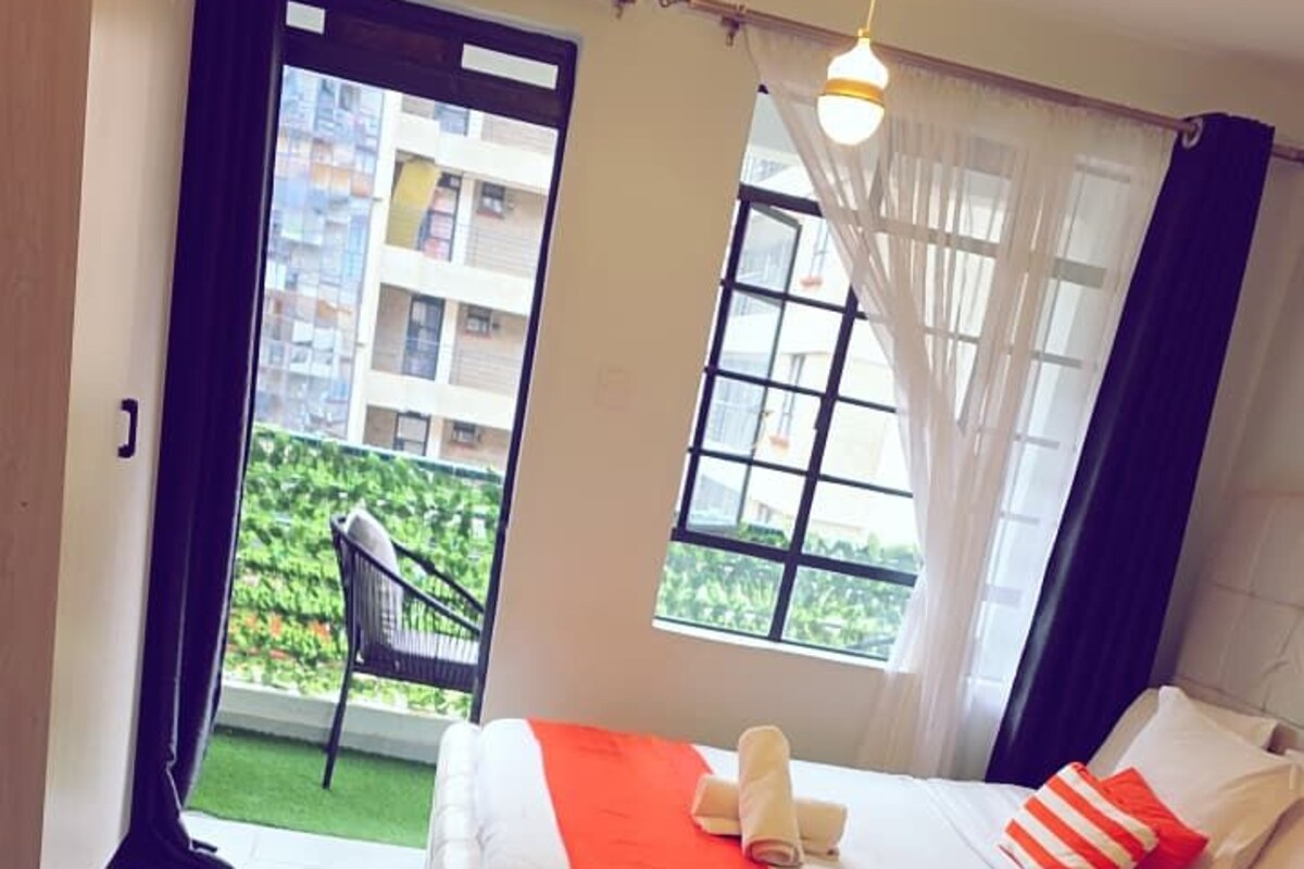 A hotel room with a bed, a small table, a chair, and a view of a balcony with a chair outside.