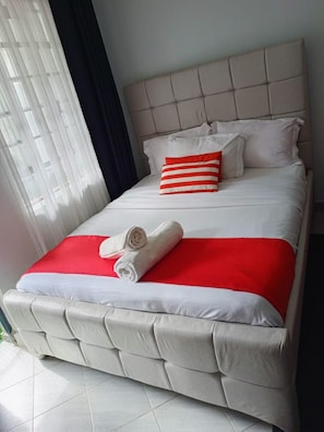 A bed with a headboard, pillows, and a red and white blanket. - Amaziah Apartments Muthiga (Rungiri)