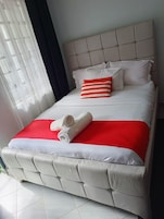 Una cama con cabecera, ropa de cama blanca y un detalle rojo.