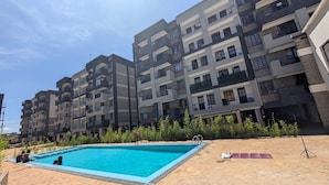 Ein Wohngebäude mit Swimmingpool, Balkonen und einer gepflasterten Fläche.