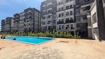 Un edificio residencial con piscina, balcones y una zona pavimentada.