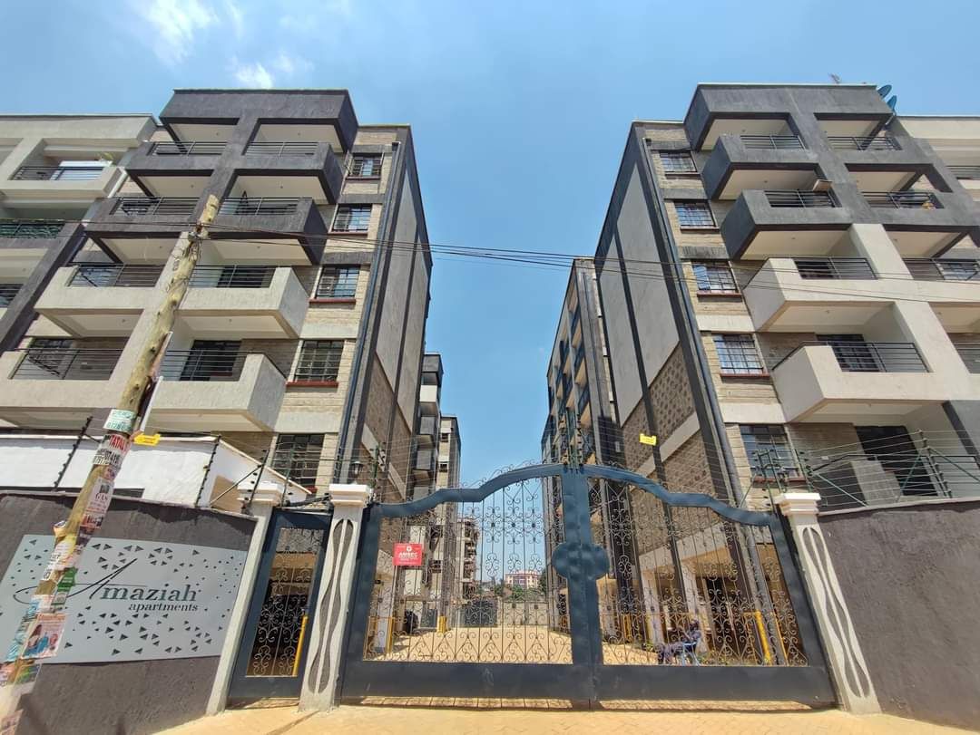 A multi-story residential building with a gated entrance, balconies, and a sign indicating 'Azmazh Apartments.'