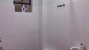 Ein Badezimmer mit weiß gefliesten Wänden, einem Fenster mit Ablage für Toilettenartikel, einem Handtuchhalter und einer Toilette.