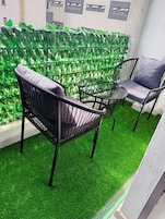 A balcony with artificial green grass, two black metal chairs, and a glass table.