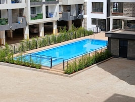 Piscina rectangular con barandilla negra, rodeada por una zona pavimentada con vegetación.