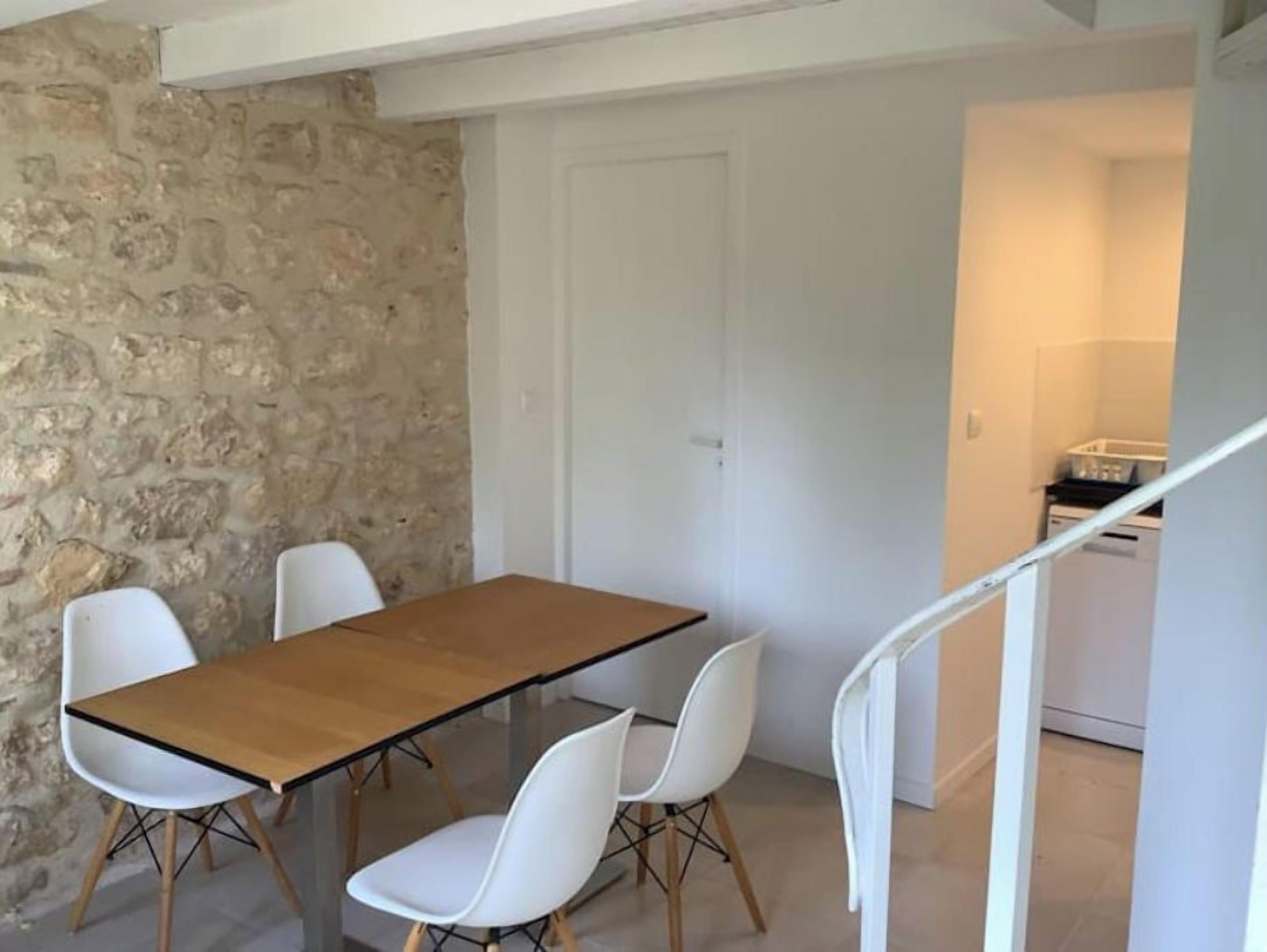 Un comedor con una mesa de madera y sillas blancas, una pared de piedra y una puerta blanca.