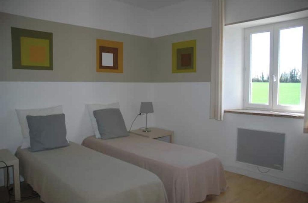 Un dormitorio con dos camas, una mesita de noche con lámpara y una ventana con vista a un campo verde.