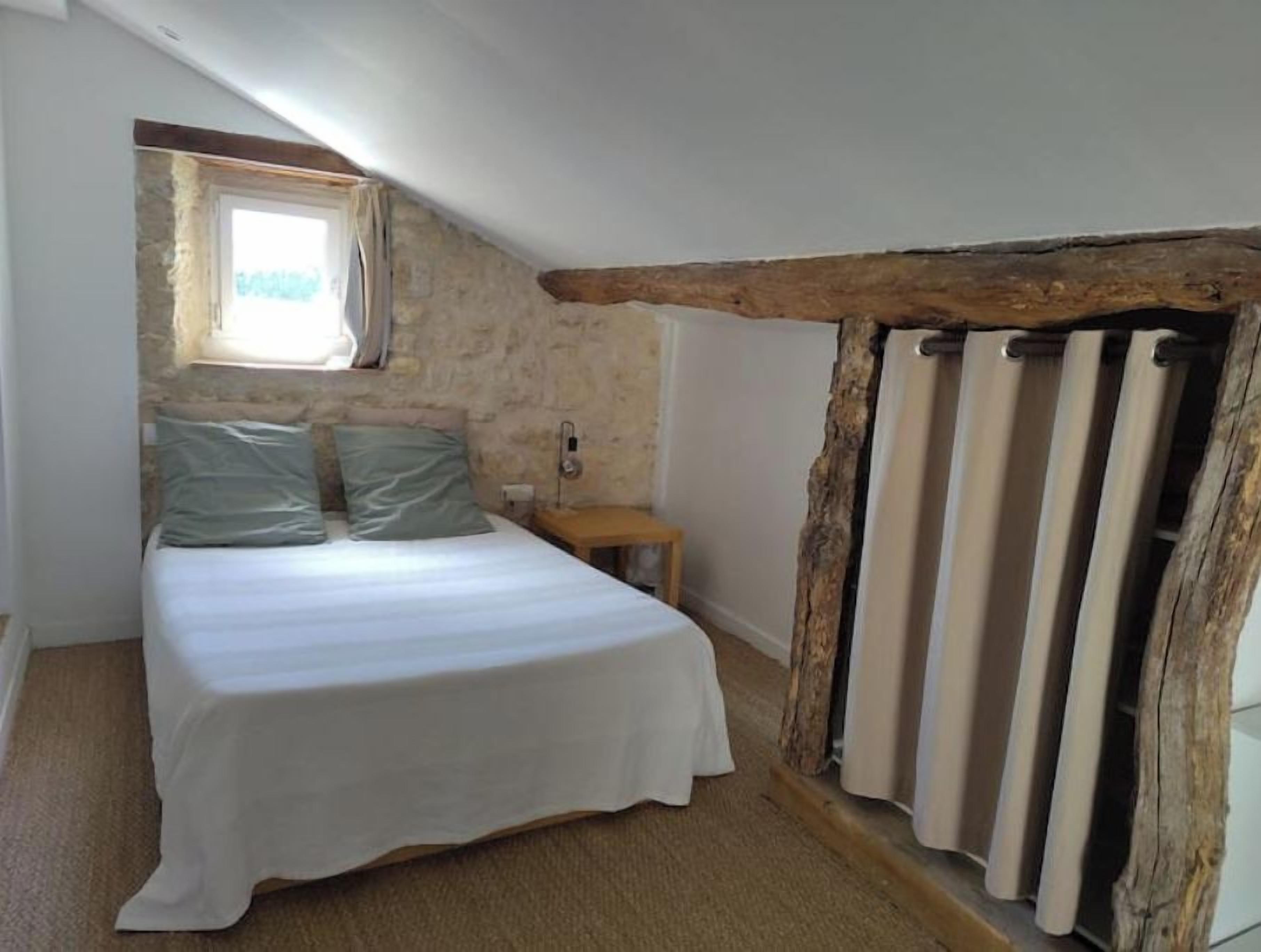 A bedroom with a bed, a small table, a window, and a rustic wooden beam.