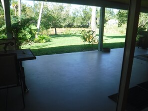 A covered patio area with a concrete floor, surrounded by greenery and trees. - Peaceful home on an enchanting private pond, minutes to everything in Vero Beach (Vero Beach)
