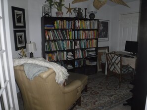A cozy living room with a beige armchair, a bookshelf filled with books, a desk with a computer, and a patterned rug. - Peaceful home on an enchanting private pond, minutes to everything in Vero Beach (Vero Beach)