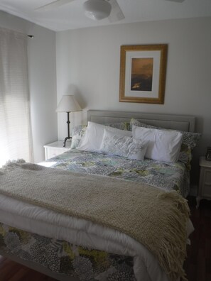 A bedroom with a bed, a nightstand, a lamp, a framed picture on the wall, and a window with curtains. - Peaceful home on an enchanting private pond, minutes to everything in Vero Beach (Vero Beach)