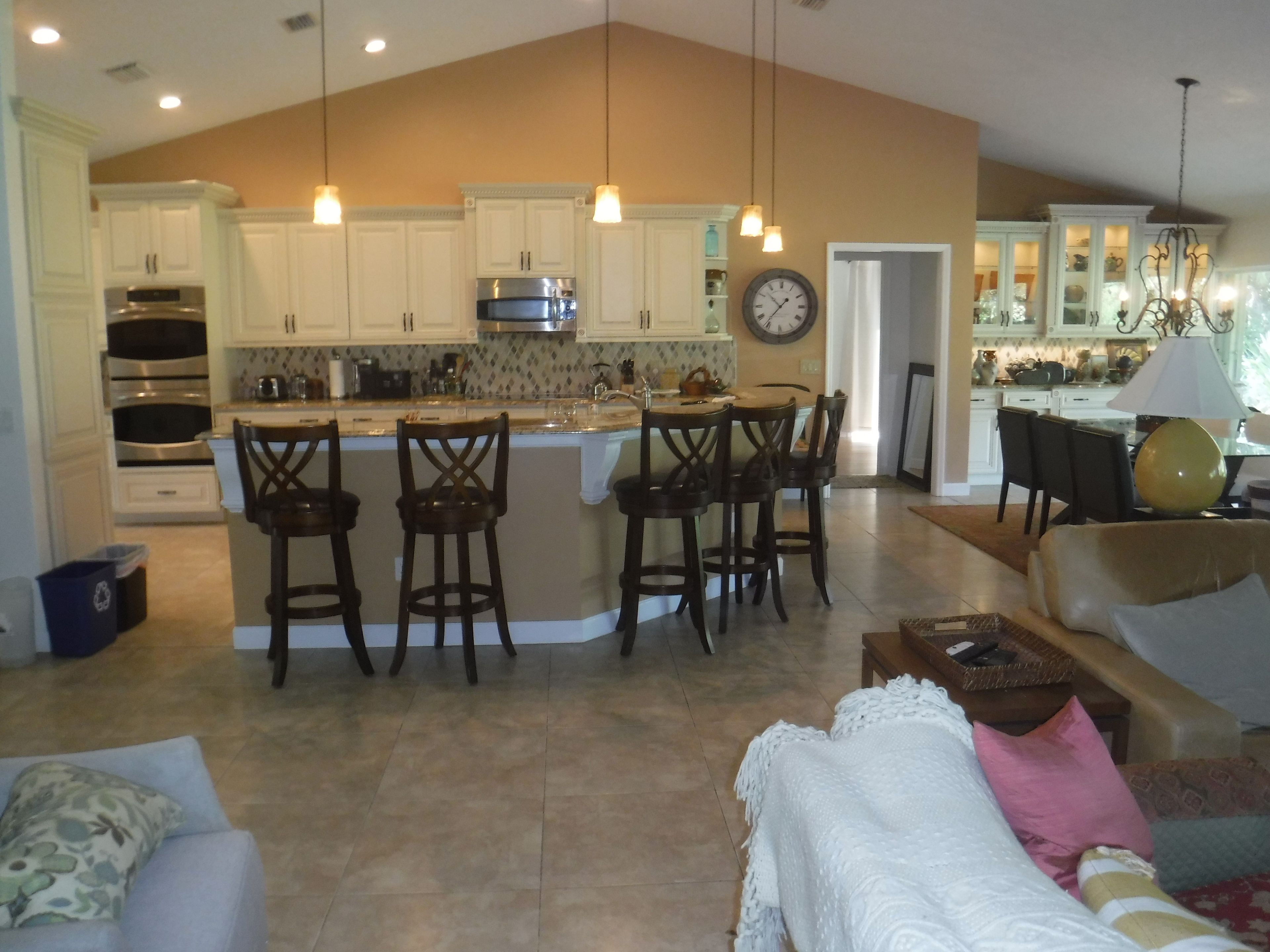 Una cuina àmplia amb armaris blancs, una illa central amb tamborets i una zona de menjador amb un penjó.