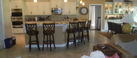 A spacious kitchen with white cabinets, a central island with bar stools, and a dining area with a chandelier.