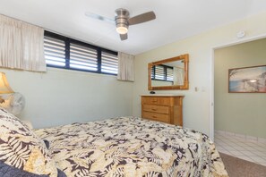 A bedroom with a bed, a ceiling fan, a window with blinds, a wooden dresser, and a painting on the wall. - Oceanfront 6th Floor - Keawakapu Beach - Pool + AC (Kihei)