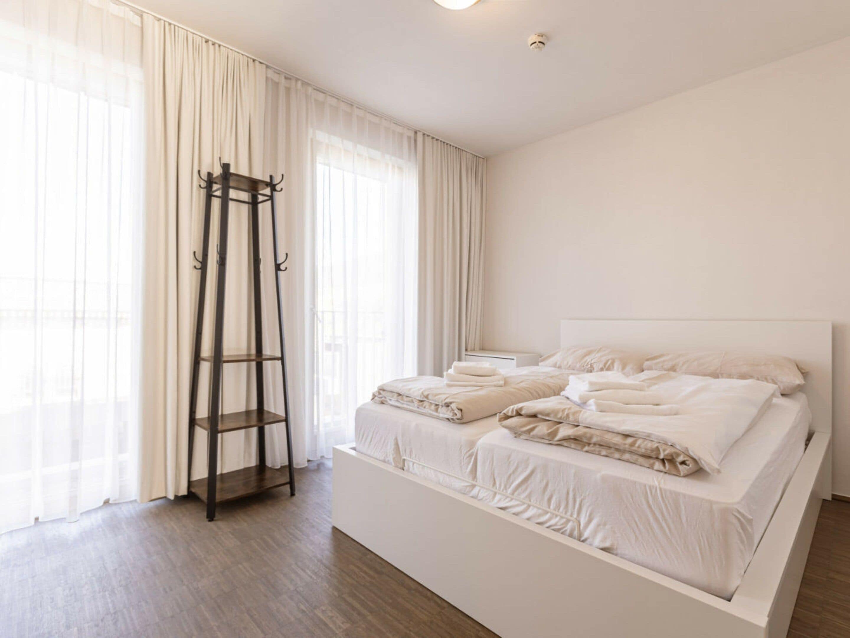 A modern bedroom with a large bed, a wooden ladder, and sheer curtains.