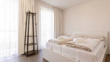 A modern bedroom with a large bed, a wooden ladder, and sheer curtains.