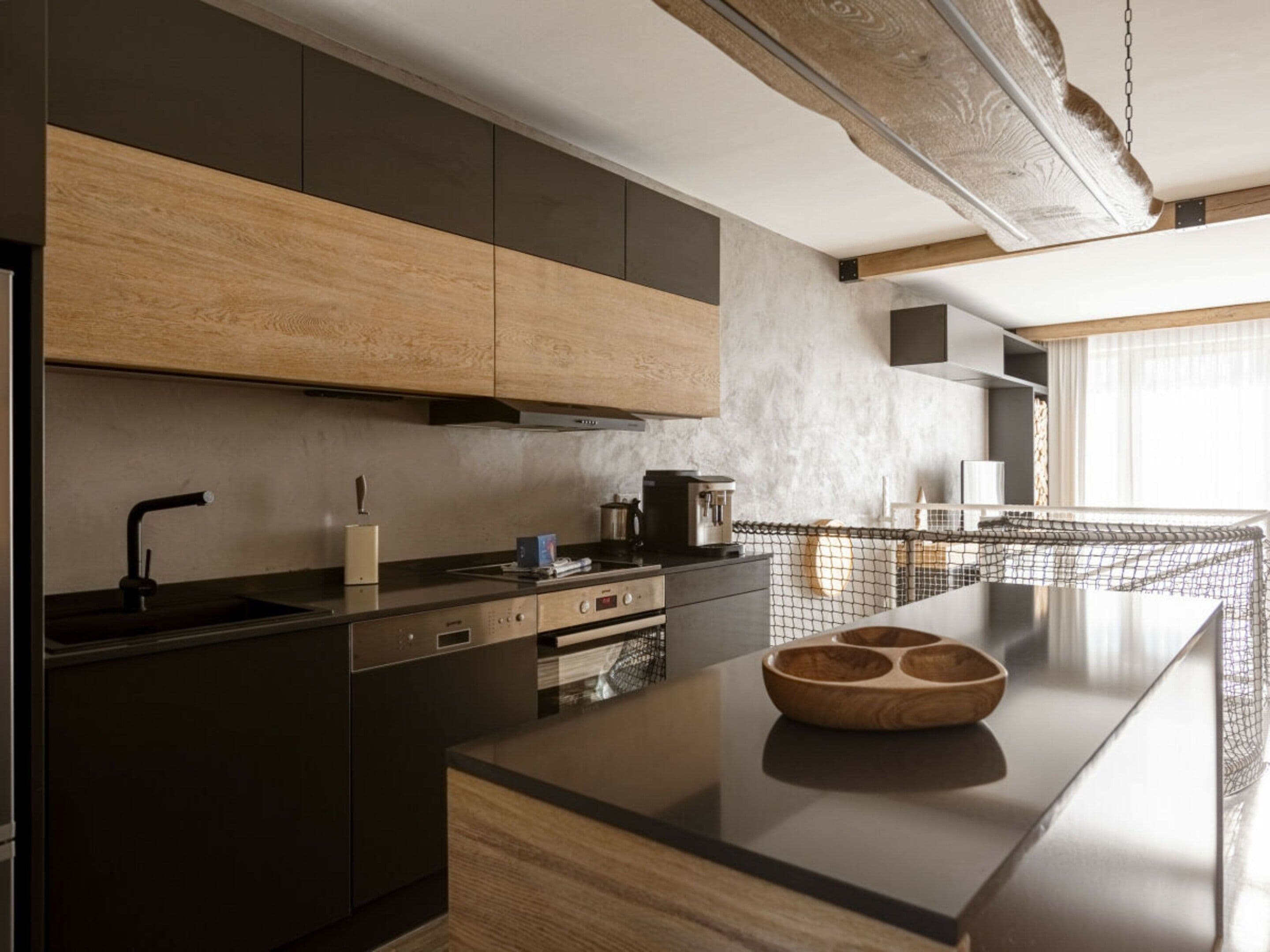 A modern kitchen with a central island, built-in appliances, and a large window providing natural light.