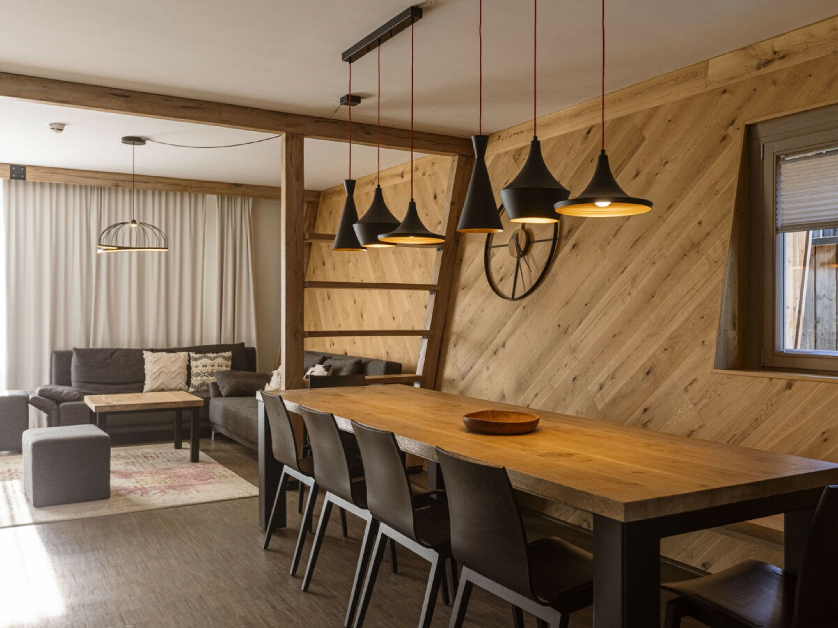 Un comedor moderno con mesa y sillas de madera, lámparas colgantes y un reloj en la pared.