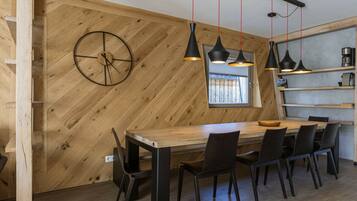 A modern dining area with a wooden herringbone wall, a round wall clock, and pendant lighting.