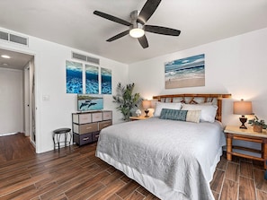 A bedroom with a bed, a ceiling fan, a nightstand, a lamp, and wall art. - Kailua-Kona, Holualoa Bay Villas, Spacious 4 BR, Beachfront, Sleeps 12 (Kailua-Kona)