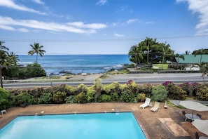 A swimming pool with lounge chairs and umbrellas, a road with a guardrail, and a view of the ocean. - Kailua-Kona, Holualoa Bay Villas, Spacious 4 BR, Beachfront, Sleeps 12 (Kailua-Kona)