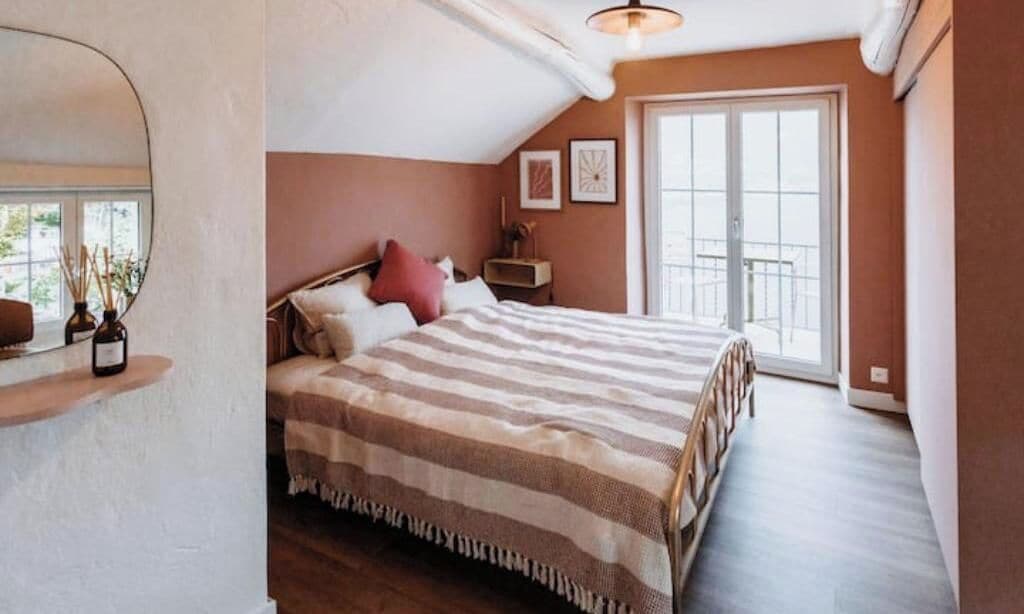 A bedroom with a bed, a nightstand, a mirror, and a window.