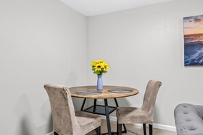 A dining area with a round table, two chairs, a vase with yellow flowers, and a painting on the wall. - Near Quantico & DC spacious, comfortable in quite area Laundry included Sleeps 6 (Woodbridge)