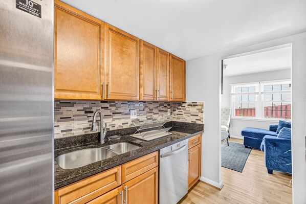A modern kitchen with wooden cabinets, a stainless steel refrigerator, a granite countertop, and a dishwasher.