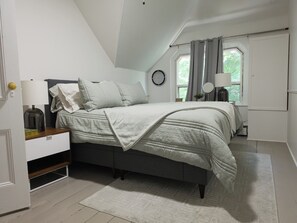 Une chambre à coucher avec un lit, des tables de chevet, une lampe, une horloge et une fenêtre avec des rideaux.