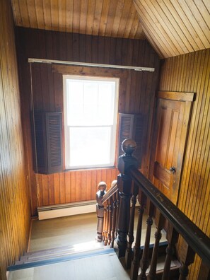 Un escalier en bois mène à une pièce dotée d’une grande fenêtre, d’une porte et d’une rambarde en bois.