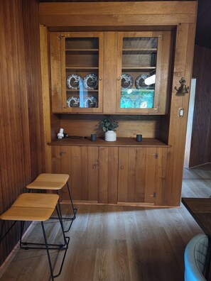 A wooden cabinet with glass doors, a small potted plant, and two foldable stools.