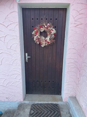 A wooden door with a wreath, a metal handle, and a concrete step leading to a door with a pink textured wall. - Casa 4 – Vacation Rental with a Panoramic View of the Lake (Vairano)