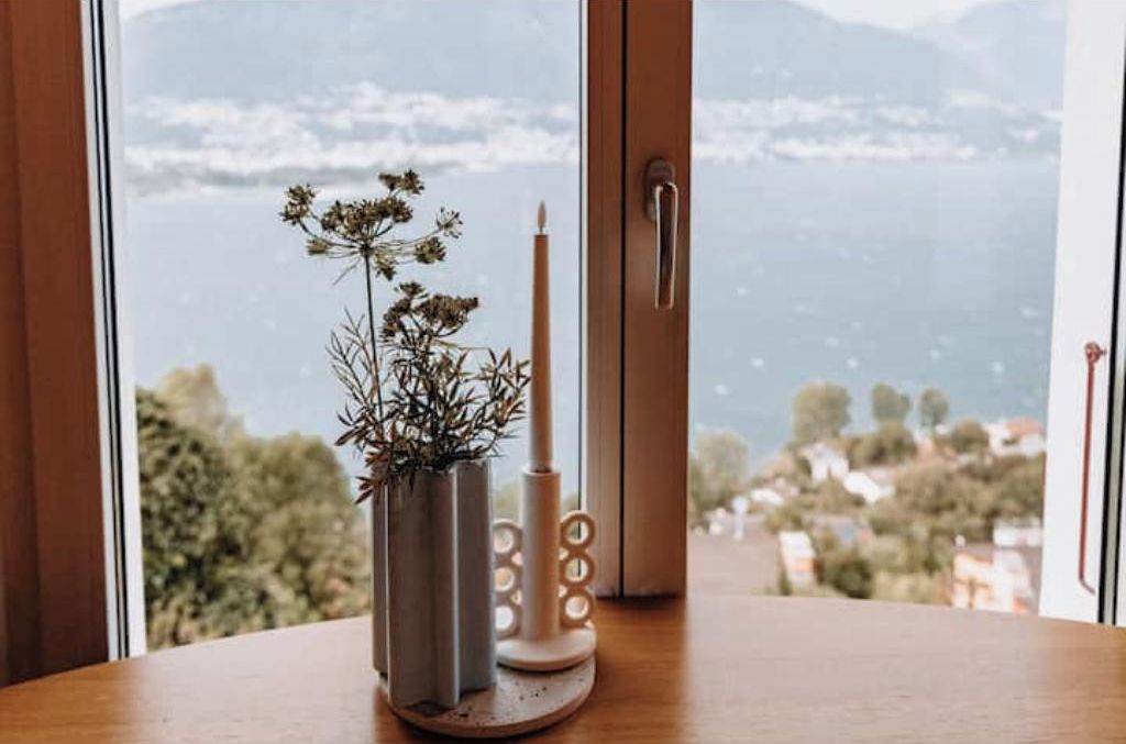Una ventana con vistas al paisaje, un candelabro y un florero con flores secas.