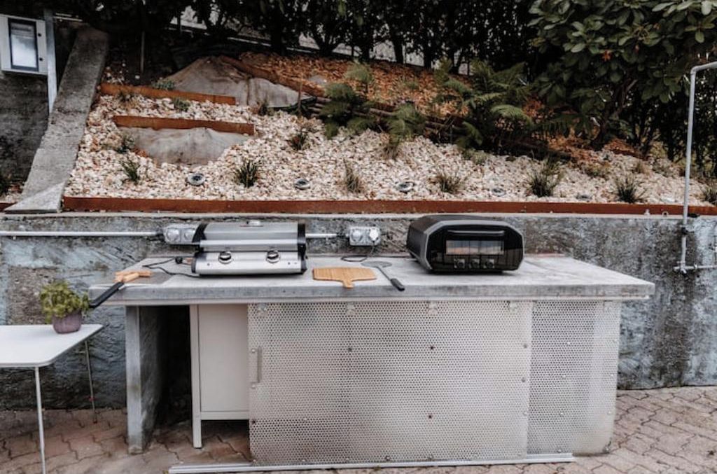 An outdoor grill station with a radio, a cutting board, and a small table with a potted plant.