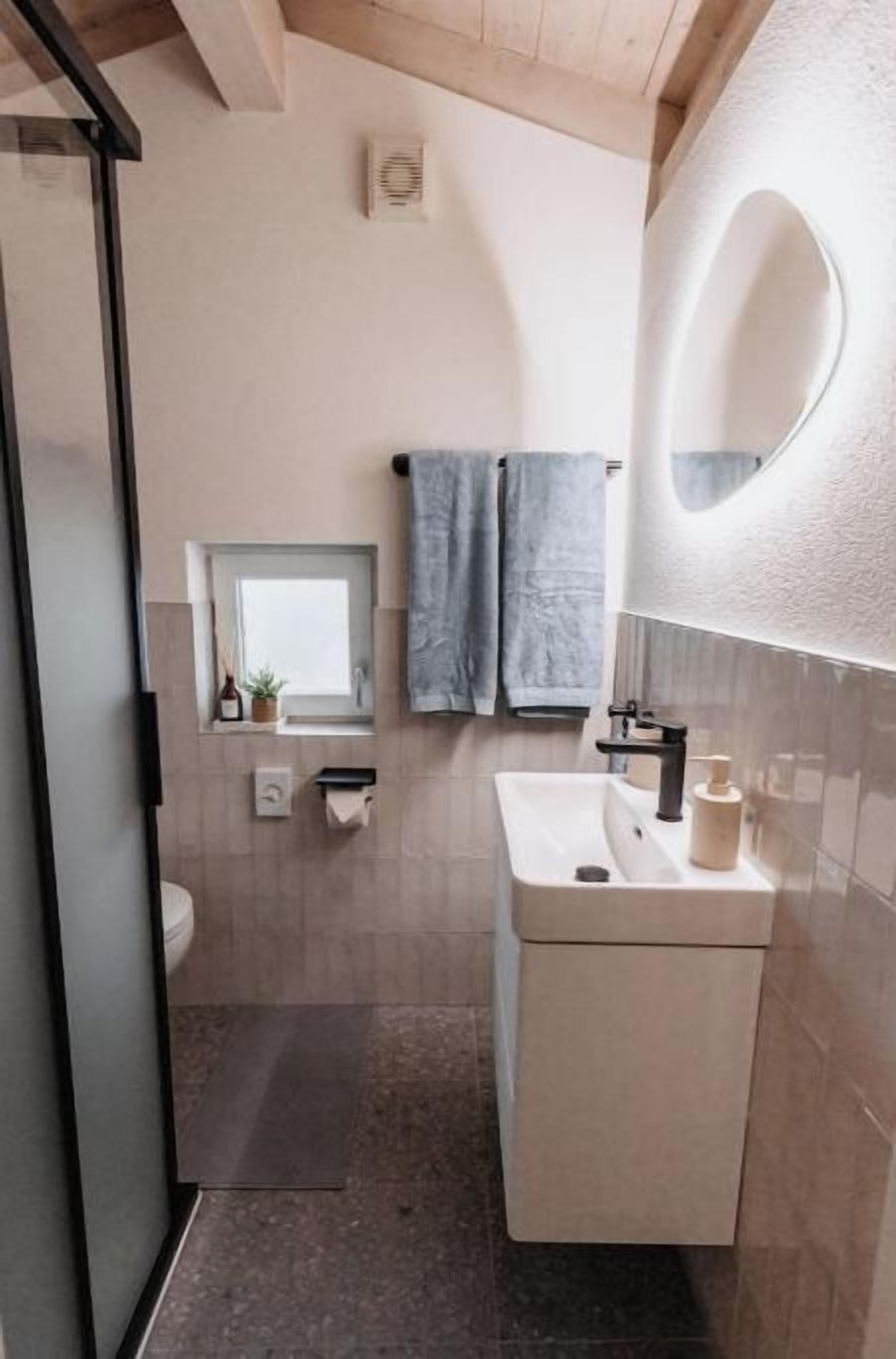 Ein modernes Badezimmer mit einer Duschkabine aus Glas, einem weißen Waschbecken und einem Spiegel mit runder Rahmung.