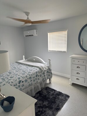 A bedroom with a bed, a dresser, a ceiling fan, an air conditioner, and a window with blinds. - Relax and Unwind (Saint James City)