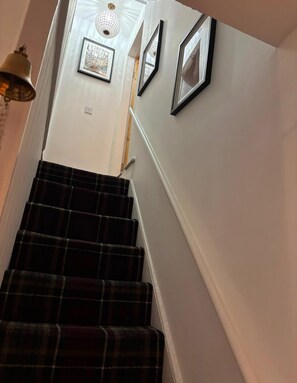 Eine Treppe mit dunkel kariertem Teppich, weißen Wänden und gerahmten Bildern an der Wand.